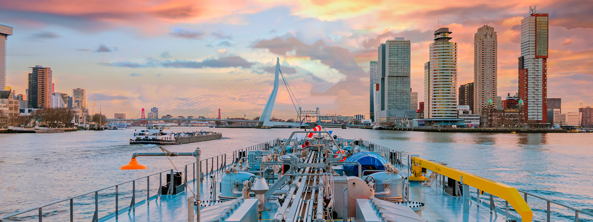 Een schip vaart de Rotterdamse Haven binnen, met zicht op de Erasmusbrug tijdens zonsondergang